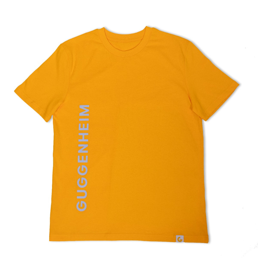The Guggenheim Constellation T-Shirt in New York Yellow is an organic cotton crewneck featuring "GUGGENHEIM" printed vertically in white on the left side, with a small white tag at the bottom right for an artful finish.