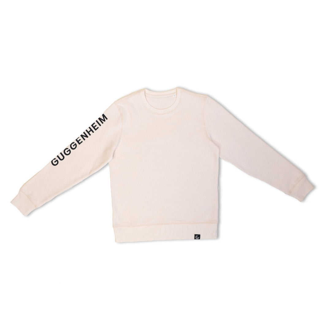 The Guggenheim Constellation Crewneck Sweatshirt in New York Natural, made from organic cotton, displays "GUGGENHEIM" in bold black on the left sleeve and is shown laid flat against a white background.