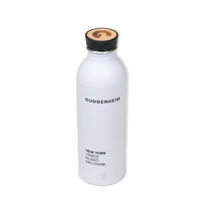 The Guggenheim Constellation Water Bottle New York is a white, recycled aluminum bottle featuring GUGGENHEIM in black, global city names beneath, and a wooden lid with a sleek black G logo.