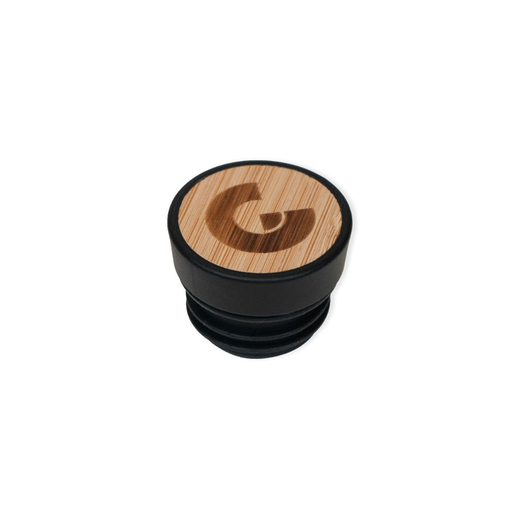 A round bottle stopper with a black base and wooden top engraved with a stylized "G," designed to complement the Guggenheim Constellation Water Bottle New York, shown in a modern style against a white background.