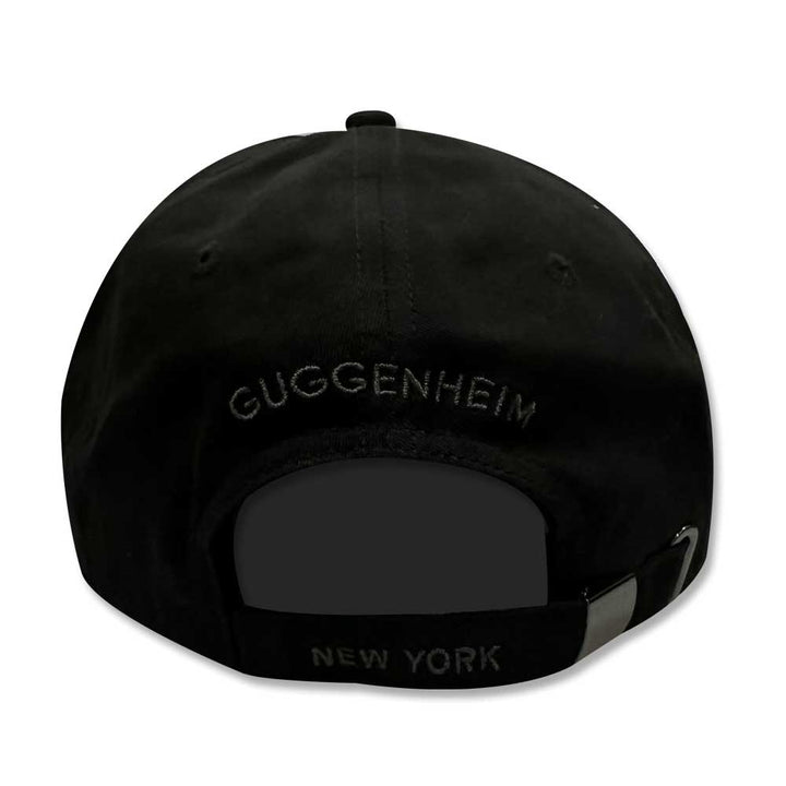The Guggenheim Going Dark Logo Cap is a black cotton cap seen from the back, with "GUGGENHEIM" embroidered above the opening and "NEW YORK" on the adjustable strap, inspired by contemporary artists.