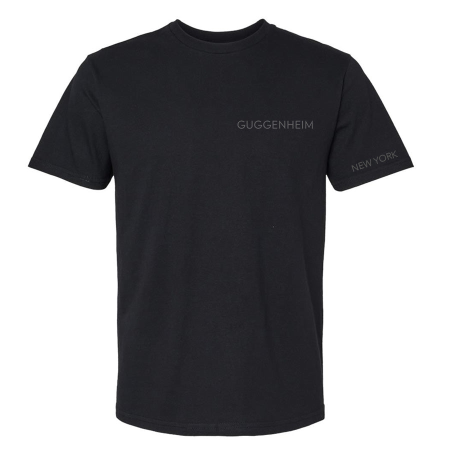 The Guggenheim Going Dark Rotunda T-Shirt is a plain black tee with “GUGGENHEIM” in small, light gray letters on the left chest and “NEW YORK” in smaller text on the left sleeve—a subtle nod to contemporary artists.