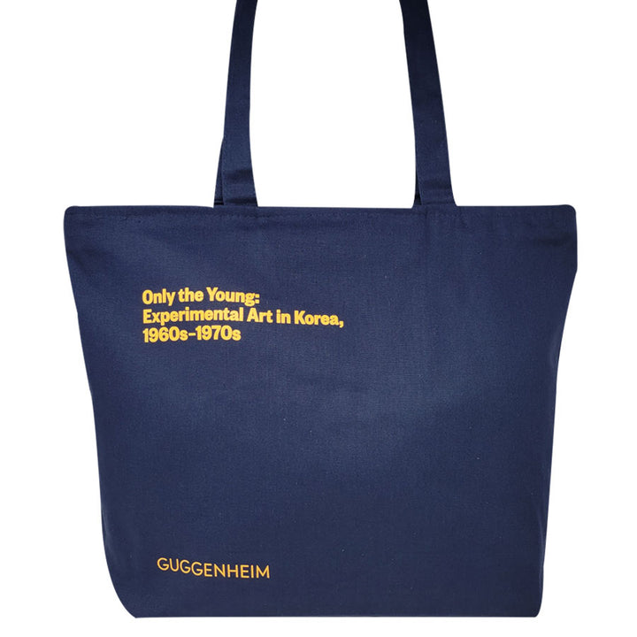 The "Only the Young: Experimental Art in Korea, 1960s-1970s" Exhibition Tote is a navy blue, heavy-duty cotton bag featuring bold yellow exhibition text and a 'Guggenheim' logo in the corner.