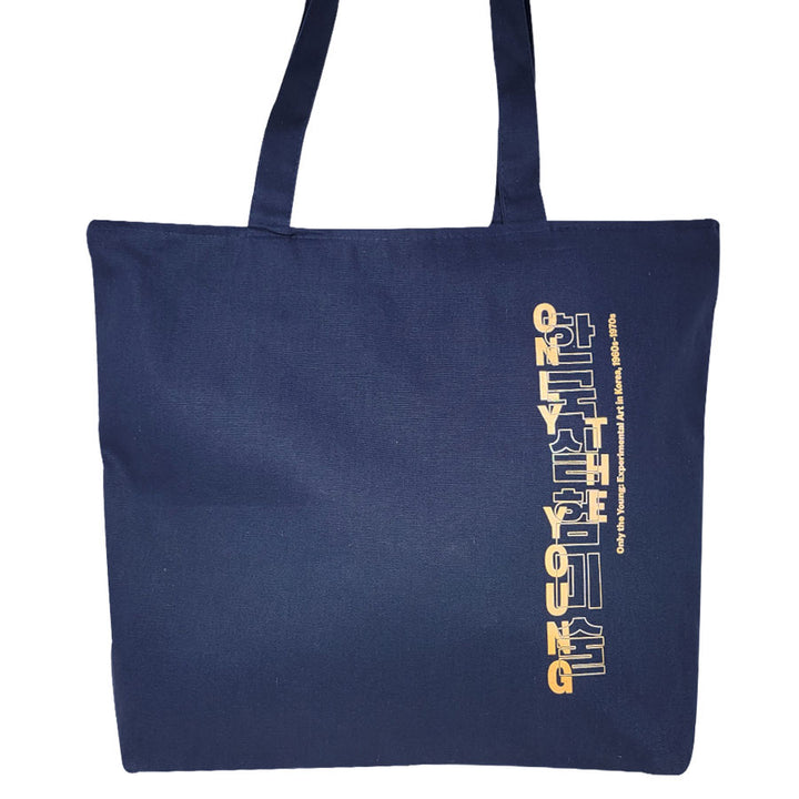 The Only the Young: Experimental Art in Korea, 1960s-1970s Exhibition Tote is a navy blue heavy-duty cotton bag with long handles and vertical yellow and white text reading STAY YOUNG on one side.