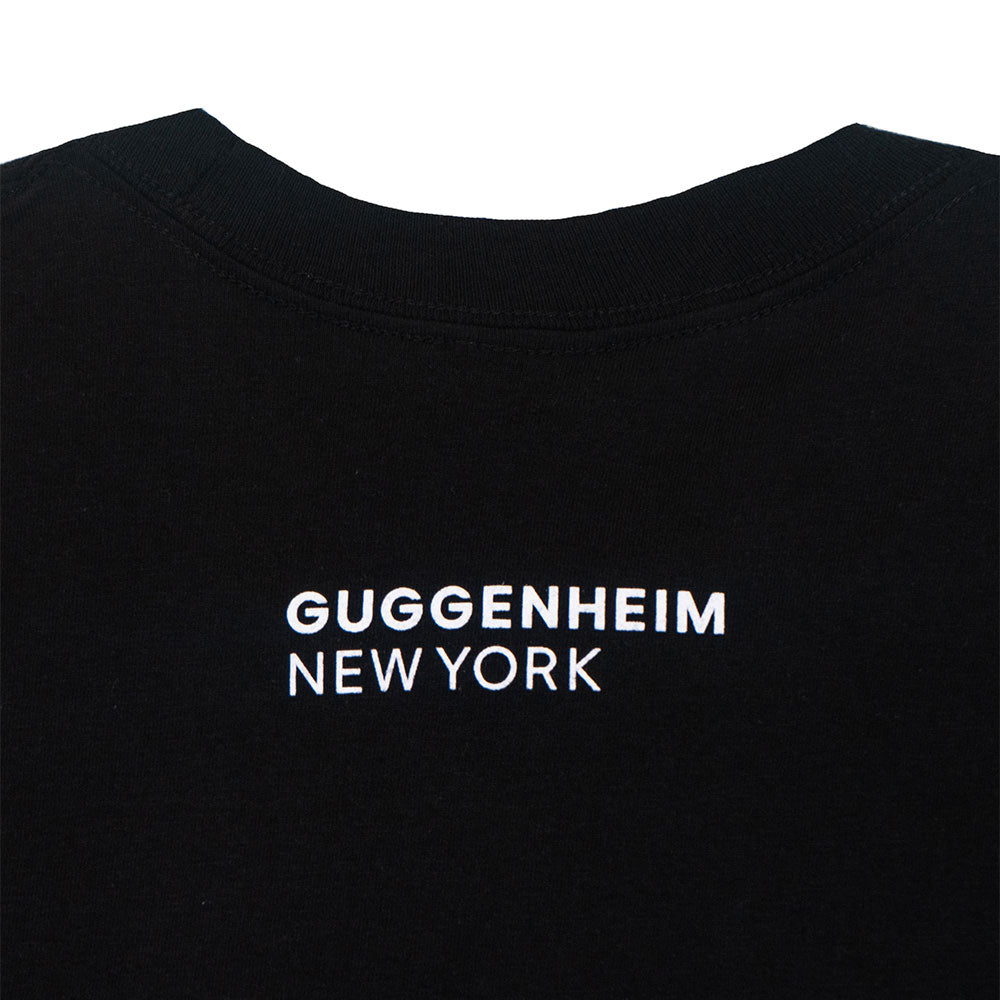A close-up of the back of the black Guggenheim Icon T-Shirt shows "GUGGENHEIM NEW YORK" in bold white letters near the neckline, celebrating iconic art and architecture.