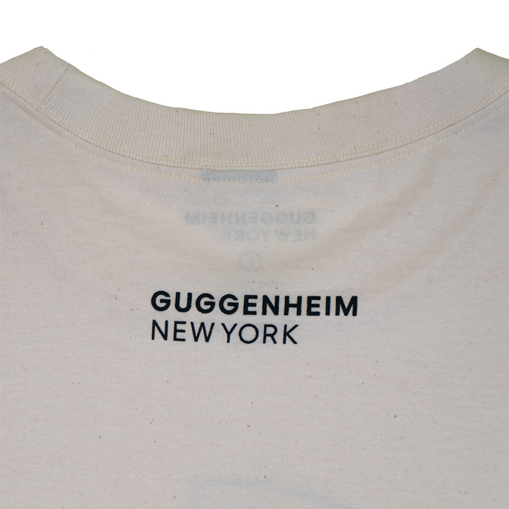 Close-up of the upper back of the Guggenheim Icon T-Shirt, Natural—a unisex cotton shirt featuring "GUGGENHEIM NEW YORK" in black near the collar, celebrating art and architecture.
