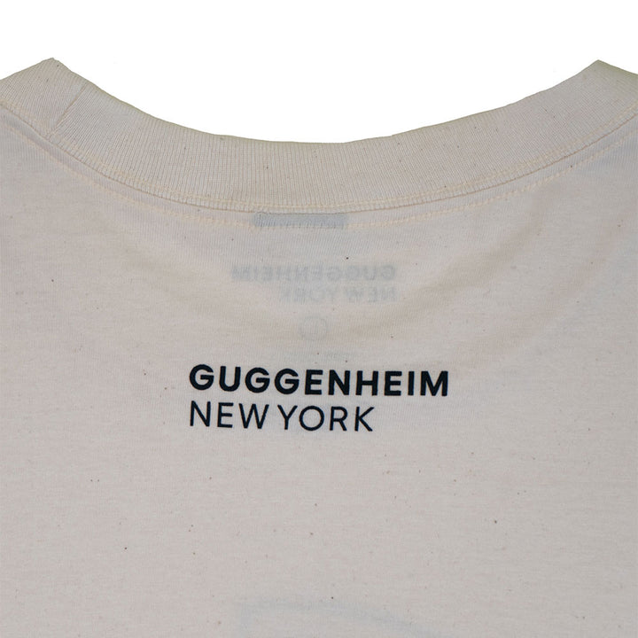 Close-up of the upper back of the Guggenheim Icon T-Shirt, Natural—a unisex cotton shirt featuring "GUGGENHEIM NEW YORK" in black near the collar, celebrating art and architecture.