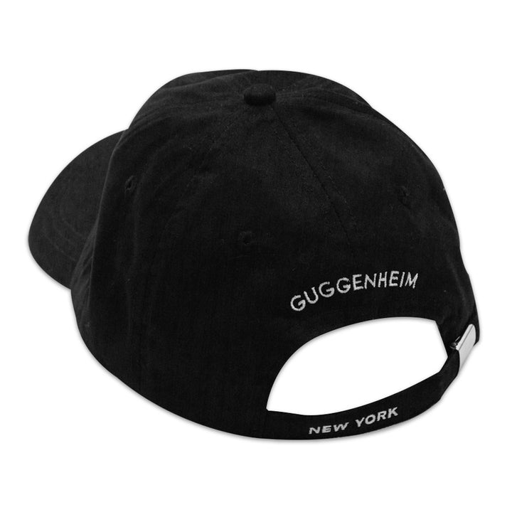 The Guggenheim "G" Cap is a black cotton adjustable baseball cap, featuring "GUGGENHEIM" embroidered in white on the back and "NEW YORK" stitched on the strap. Shown from a rear angle.