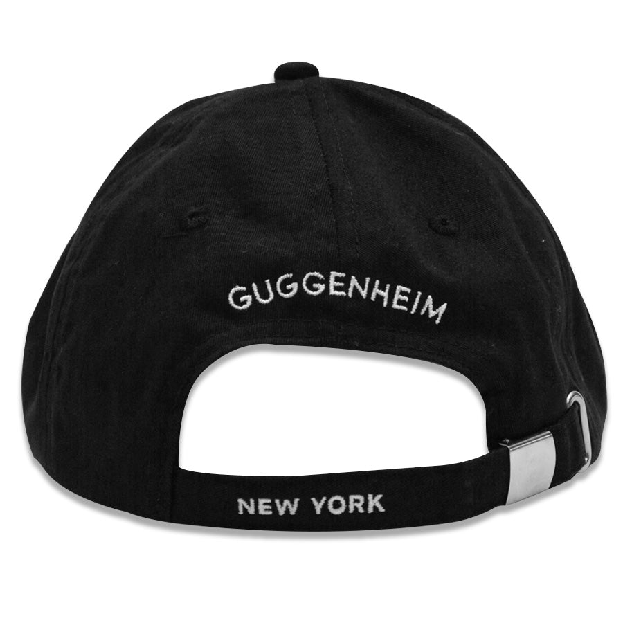 A black cotton adjustable Guggenheim "G" Cap, shown from the back, with "GUGGENHEIM" embroidered in white above the opening and "NEW YORK" stitched in white on the strap.