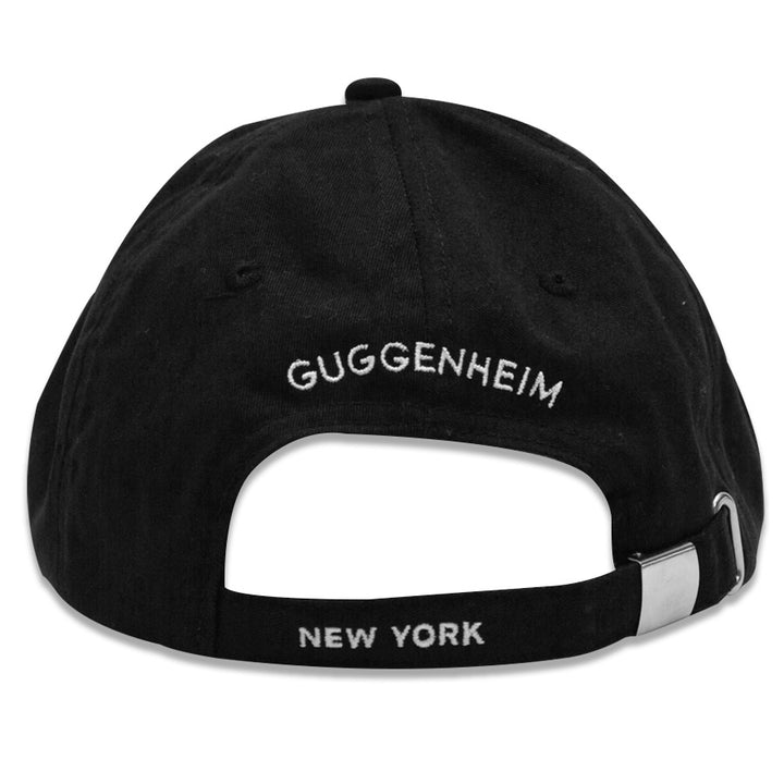 A black cotton adjustable Guggenheim "G" Cap, shown from the back, with "GUGGENHEIM" embroidered in white above the opening and "NEW YORK" stitched in white on the strap.