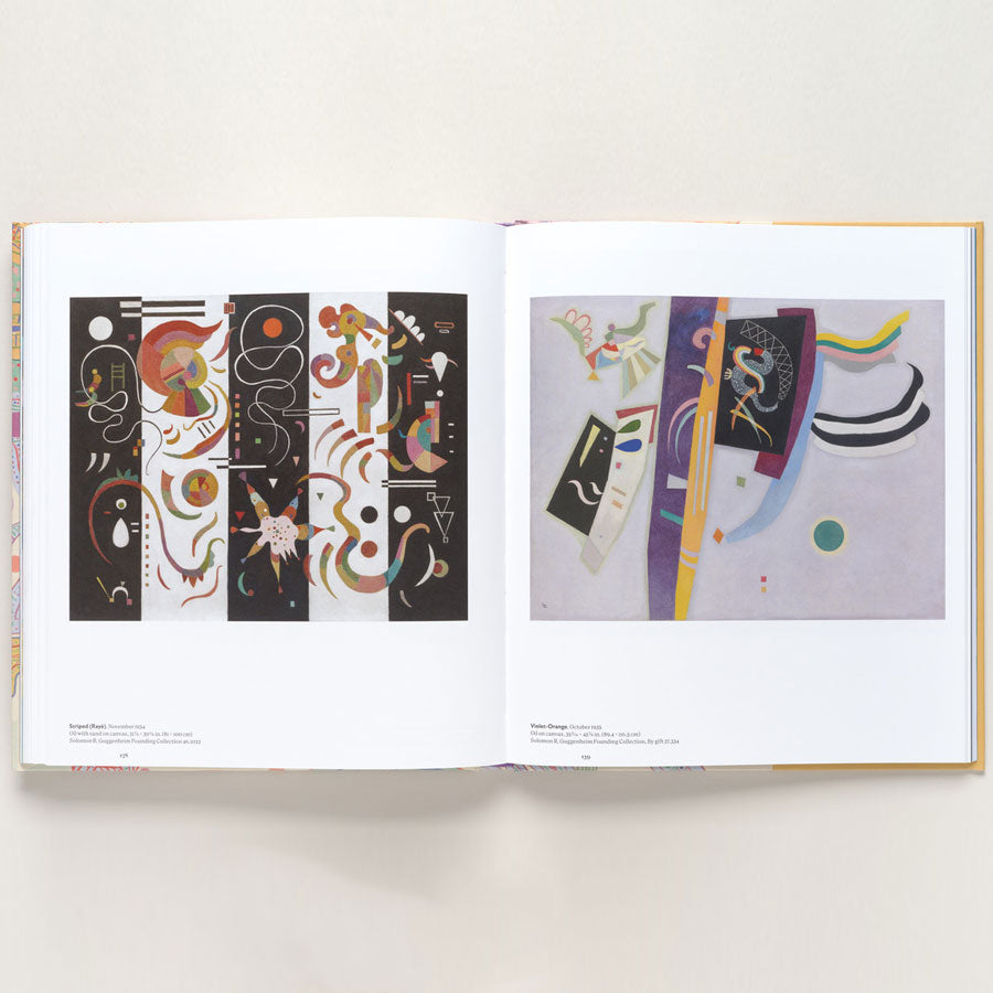 The open book "Vasily Kandinsky: Around the Circle" features two abstract, geometric, and vibrantly colored paintings on white pages, inspired by Bauhaus and European modernism, set against a simple light background.