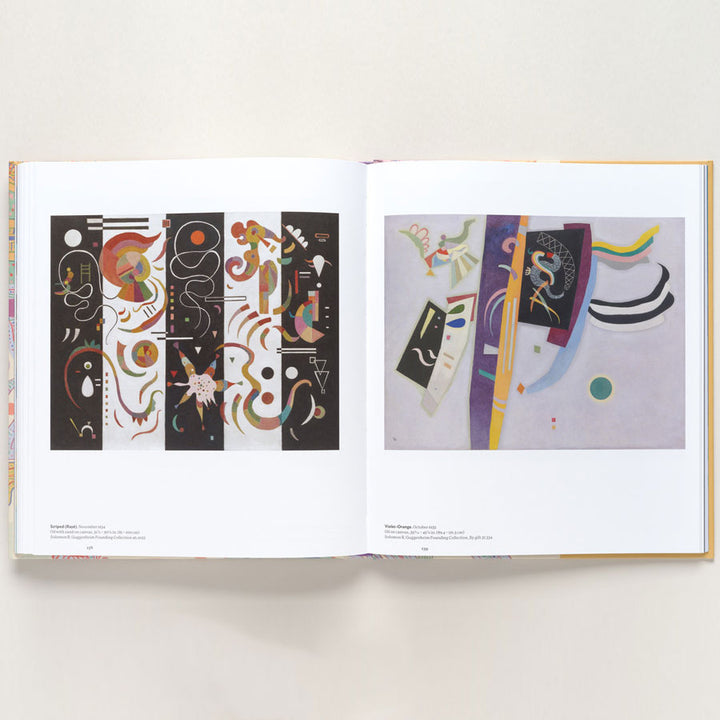 The open book "Vasily Kandinsky: Around the Circle" features two abstract, geometric, and vibrantly colored paintings on white pages, inspired by Bauhaus and European modernism, set against a simple light background.