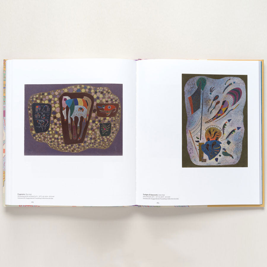 An open book from "Vasily Kandinsky: Around the Circle" shows two abstract, colorful paintings inspired by European modernism on white-bordered pages with captions—organic shapes on purple left, swirling forms and lines right.