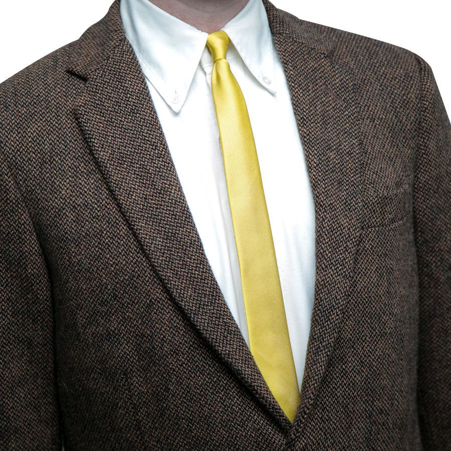 A person in a brown textured suit jacket, white dress shirt, and a bright yellow Alex Katz Limited-Edition Tie. Only the upper torso is visible, with the head partially out of frame.