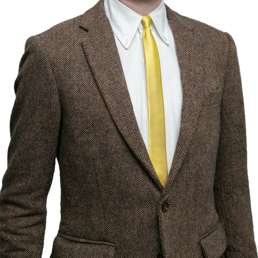 A person wearing a brown textured suit jacket, white dress shirt, and the Alex Katz Limited-Edition Tie is shown from shoulders to waist against a white background. The person's face is not visible.