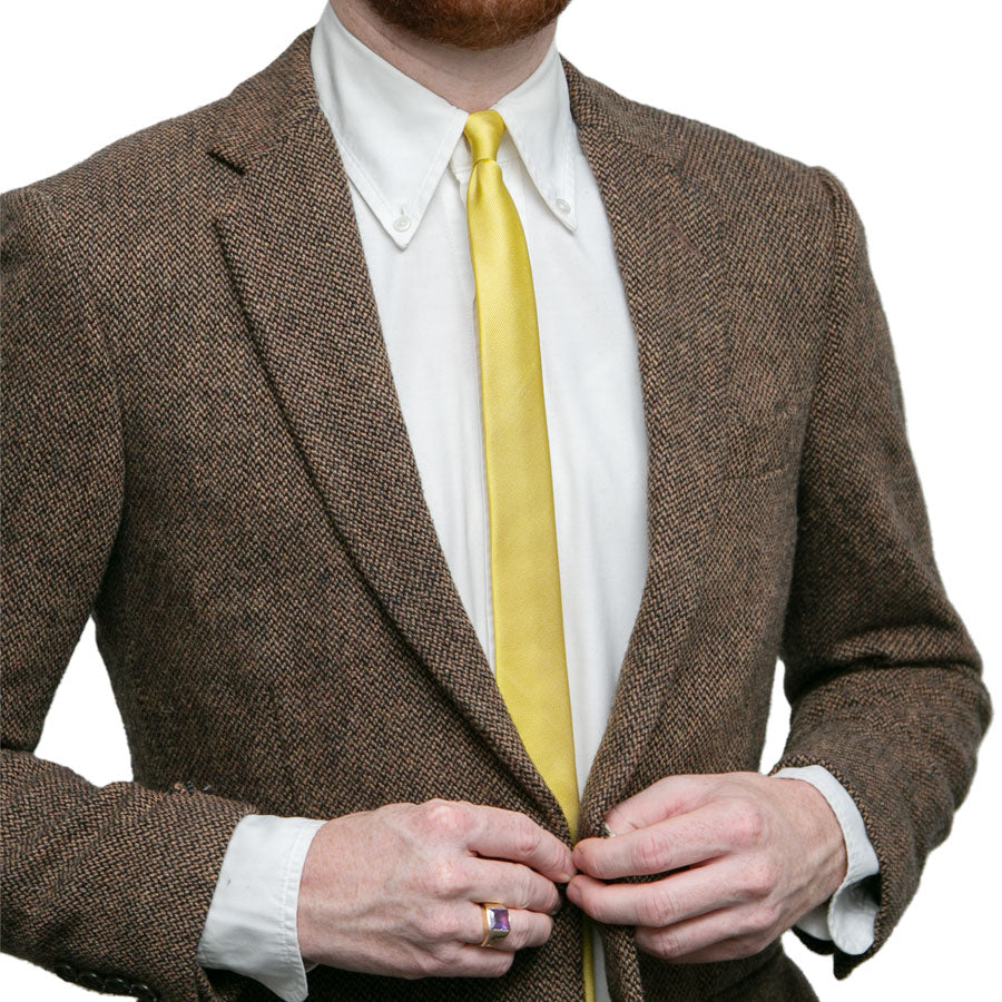 A man, face unseen, buttons his brown tweed suit jacket over a white dress shirt and the Alex Katz Limited-Edition Tie.