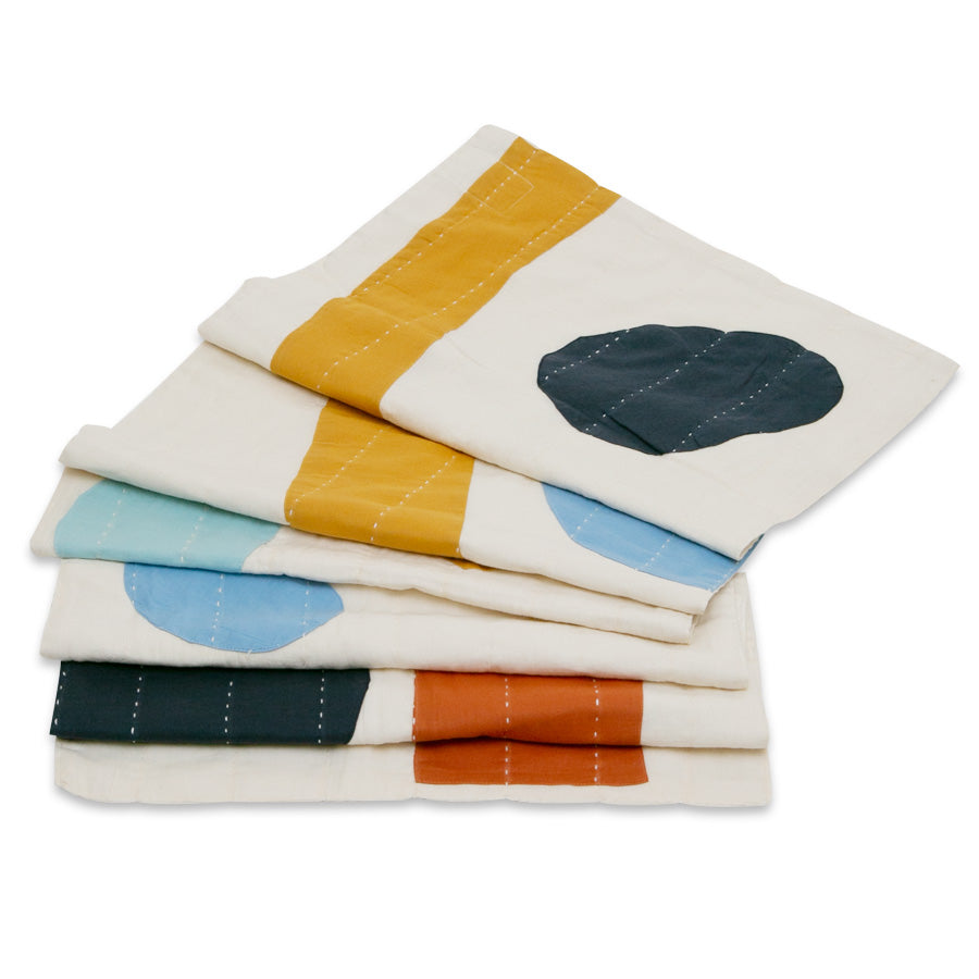 A folded cream-colored Scarf Sunrise from the Alex Katz Inspired Capsule Collection, featuring blue, yellow, orange, and black geometric shapes on GOTS certified organic cotton with visible white stitching.