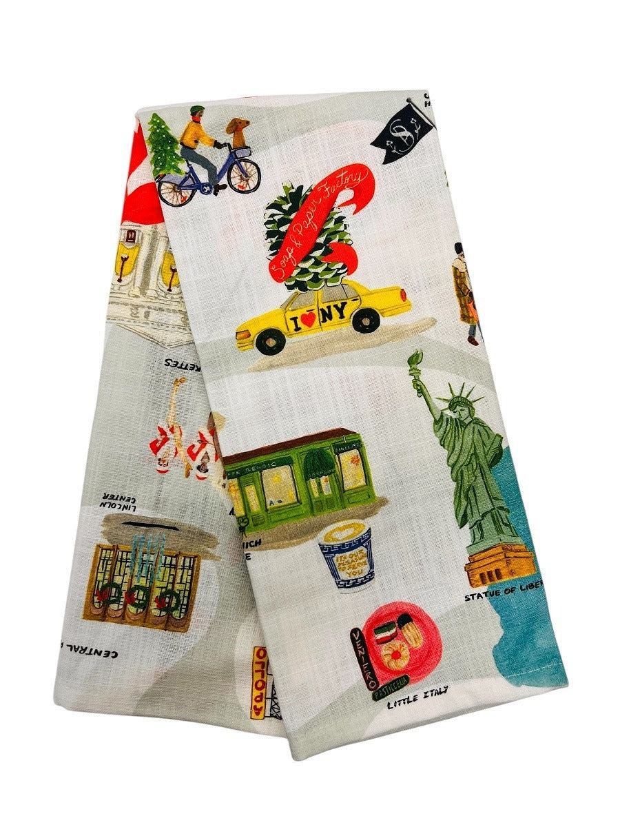 The Holiday in New York Tea Towel is a folded, phthalate-free tea towel featuring colorful illustrations of NYC landmarks and icons like the Statue of Liberty, yellow taxi, subway car, and city scenes on a light background.