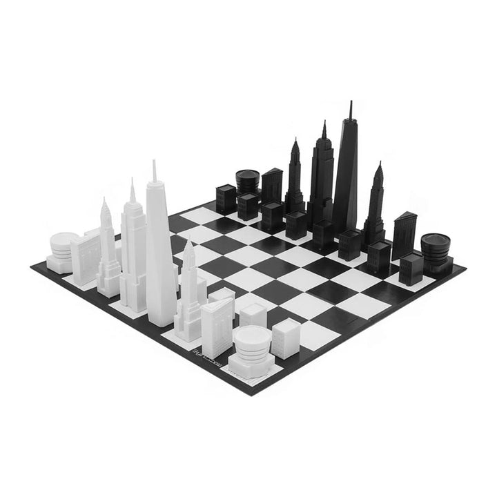 The New York City Edition - Chess Set features acrylic chess pieces in black and white, shaped like iconic skyscrapers and landmarks from the NYC skyline, replacing traditional chess pieces.
