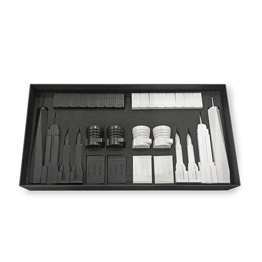 The New York City Edition - Chess Set features black and white acrylic chess pieces shaped like iconic skyscrapers, all neatly arranged in a rectangular box.