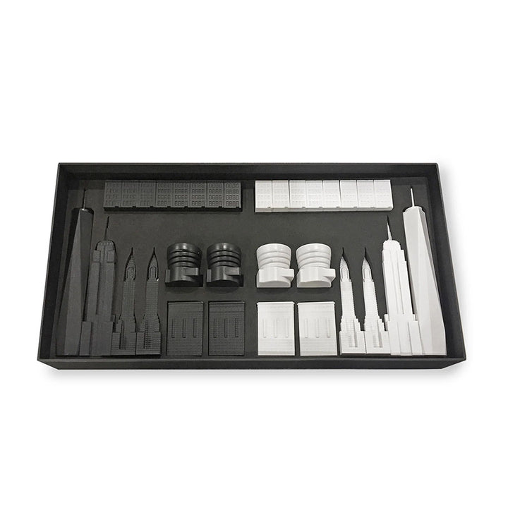 The New York City Edition - Chess Set features black and white acrylic chess pieces shaped like iconic skyscrapers, all neatly arranged in a rectangular box.