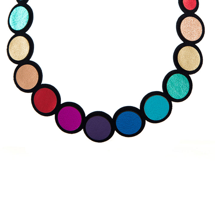 The Rainbow Circles Necklace by Iskin Sisters features lightweight circular beads in a gold-to-green gradient, arranged in a semicircle for an eye-catching look.