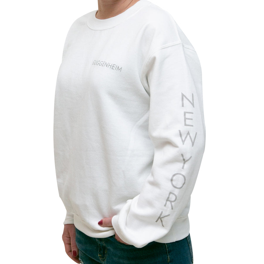 A person wears a unisex Guggenheim Rotunda Sweatshirt with "NEW YORK" printed vertically on the sleeve, posing against a plain white background.